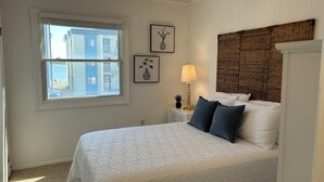 Une chambre avec un grand lit, une fenêtre et une lampe fixée au mur.