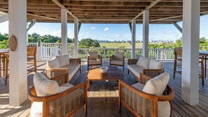 A covered outdoor seating area with wicker furniture and a view of a residential neighborhood. - Hobbs Realty - "Holden Views" a Lovely Marsh Luxury Property with Views, Views, Views! (Holden Beach)