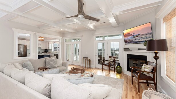 A spacious living room with a large sofa, a fireplace, a television, and a view of the city through large windows. - Hobbs Realty - "Holden Views" a Lovely Marsh Luxury Property with Views, Views, Views! (Holden Beach)