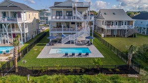 A large, multi-story residential building with a central swimming pool, multiple balconies, and a well-maintained lawn. - Hobbs Realty - "Holden Views" a Lovely Marsh Luxury Property with Views, Views, Views! (Holden Beach)