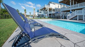 A poolside area with lounge chairs, a pool, and a building with multiple decks and outdoor seating. - Hobbs Realty - "Holden Views" a Lovely Marsh Luxury Property with Views, Views, Views! (Holden Beach)