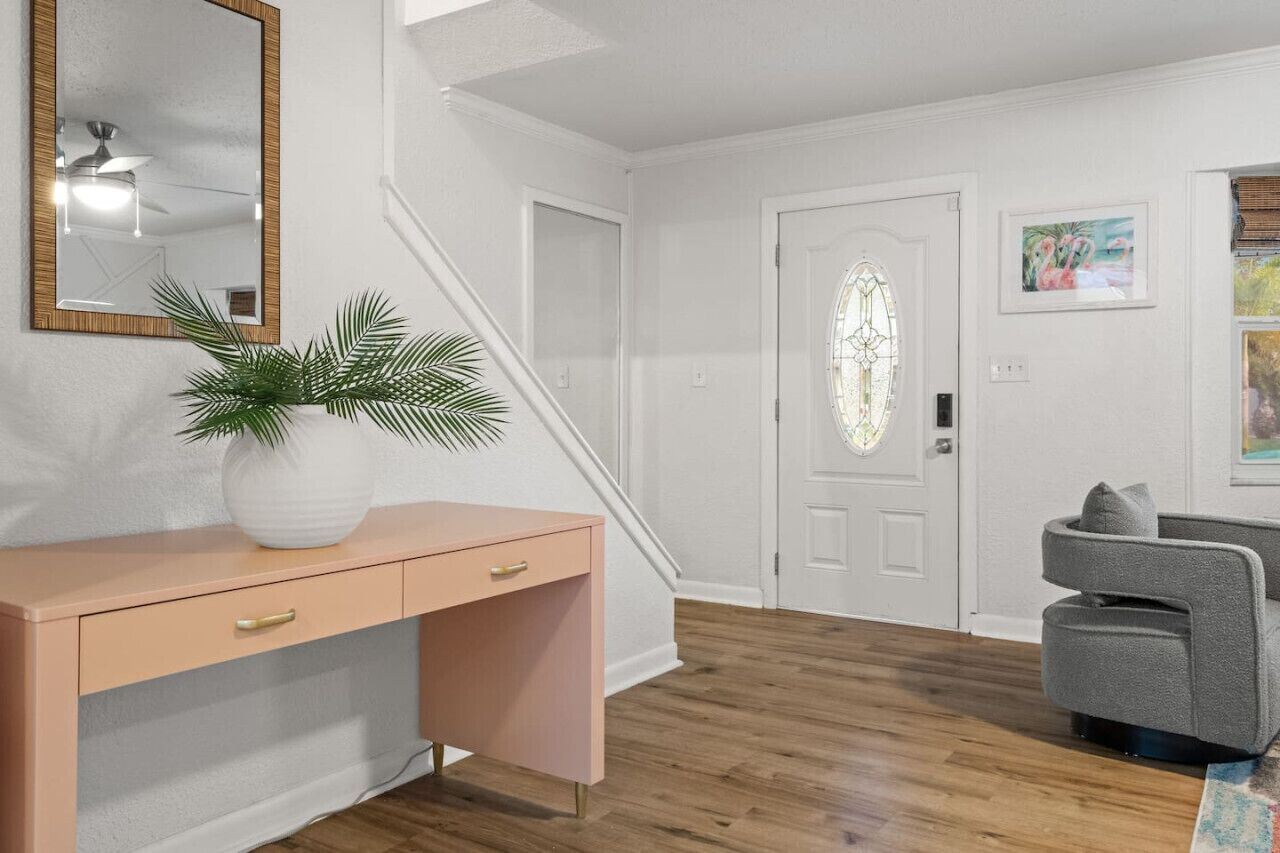 A hallway with a white door, a mirror, a desk with drawers, and a gray armchair.