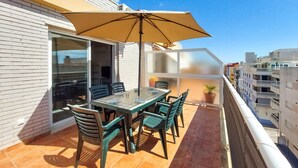 Un balcon avec une table et des chaises en verre, un parasol beige et une vue sur la ville.