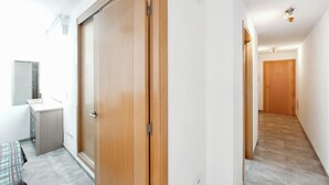 Un couloir avec une porte en bois, un miroir et un petit meuble.