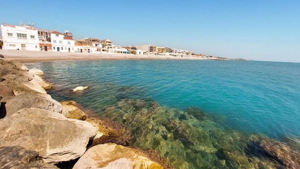 Une ville côtière avec des bâtiments qui bordent la plage, une eau d’un bleu limpide et une côte rocheuse.