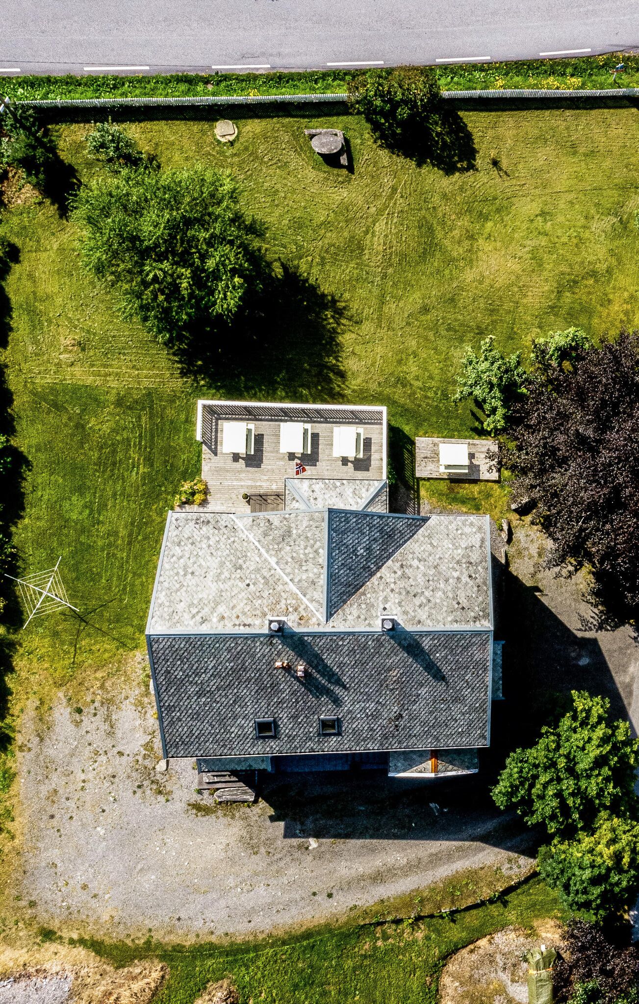 Luchtbeeld van een gebouw met een schuin dak, een klein bijgebouw en een verzorgd gazon met bomen en struiken.