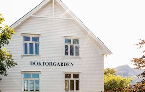 A white building with the name "DOKTORGARDEN" on the facade, featuring multiple windows and a mountainous backdrop.