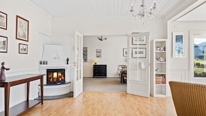 Een ruime woonkamer met een open haard, houten vloeren en uitzicht op de omgeving door een groot raam.