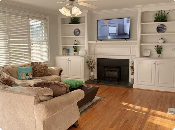 A living room with a beige sofa, a fireplace, a television mounted above the fireplace, and wooden flooring. - Beautiful and convenient house (Duncan)