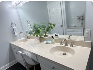 A bathroom with two sinks, a large mirror, a potted plant, and a white chair. - Beautiful and convenient house (Duncan)