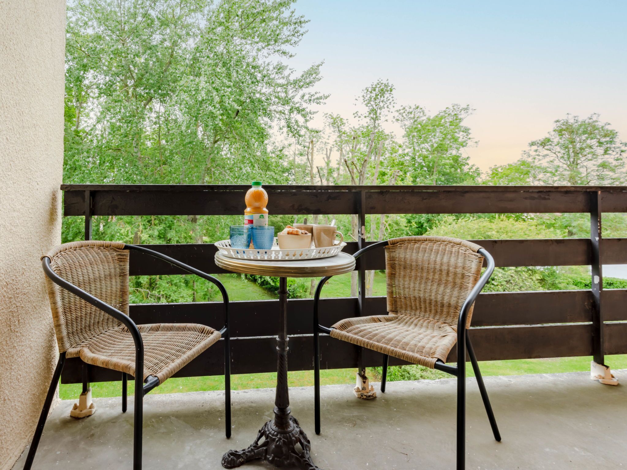 A balcony with wicker chairs, a small round table, and a tray with a beverage and snacks.