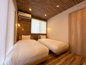 A bedroom with two beds, wooden flooring, a ceiling with recessed lighting, an air conditioning unit, and a window with blinds. - Mt Fuji Resort Club -Green- (Fujikawaguchiko)