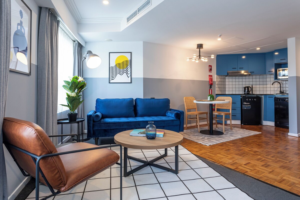 A modern living room with a blue sofa, a brown leather chair, a round coffee table, and a small side table with a plant.