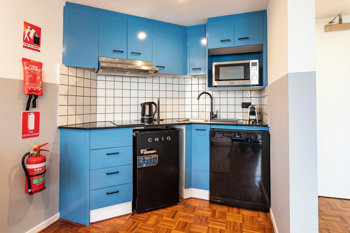 A compact kitchen with blue cabinets, a microwave, a dishwasher, and a fire extinguisher.