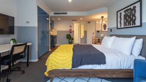 A modern hotel room with a large bed, a desk, and a chair. There is a bathroom visible in the background. - GIA Sydney  (Sydney)