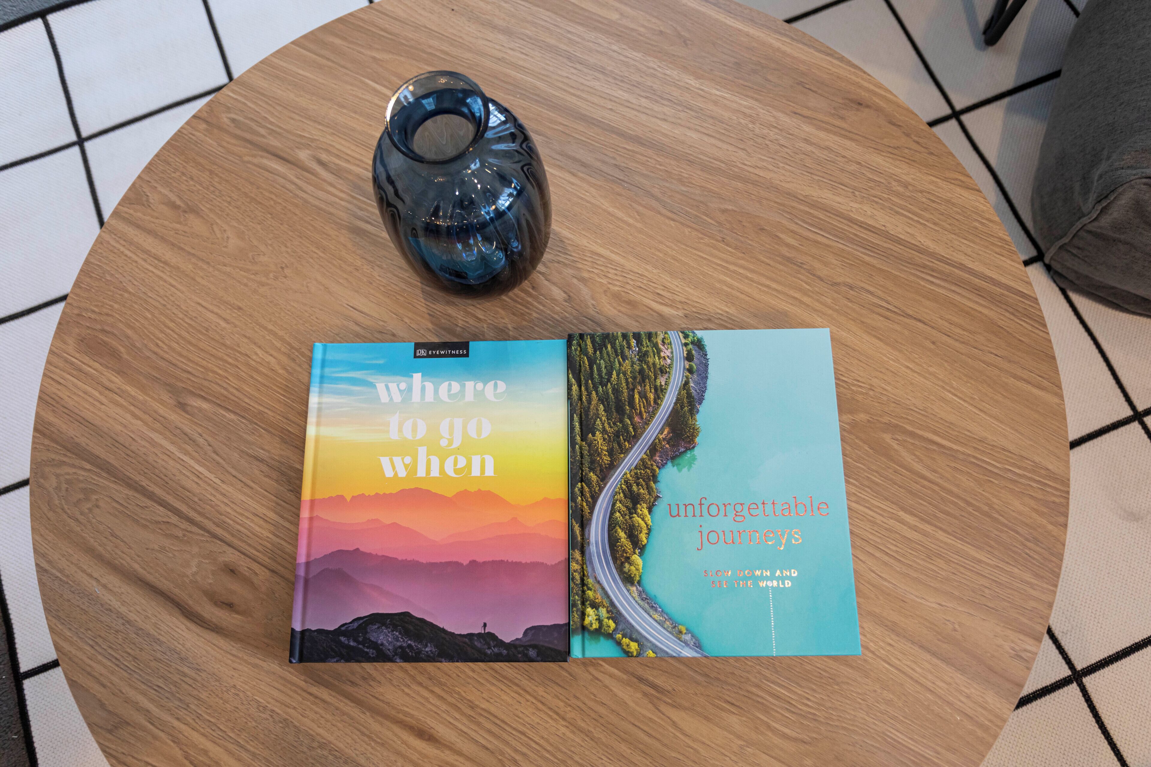 Zwei Bücher, eines mit dem Titel "Where to go when" und das andere "unforgettable journeys", liegen auf einem runden Holztisch.