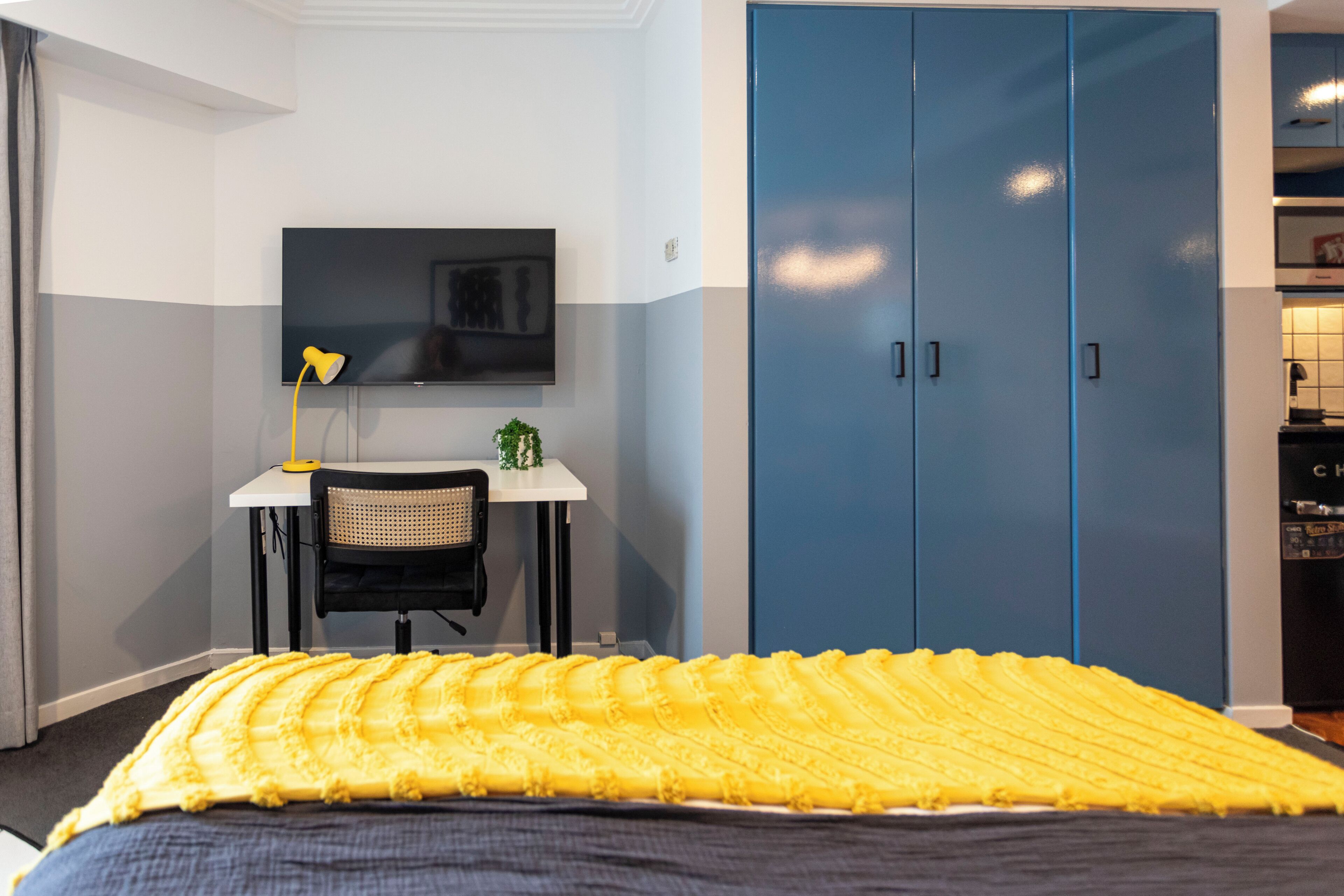 A bedroom with a bed, a desk with a chair, a TV, and blue wardrobes.