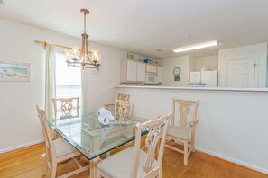 A dining area with a glass table and wooden chairs, a chandelier, a kitchen with white cabinets, and a clock on the wall. - The Fairways At River Oaks Unit D (Myrtle Beach)