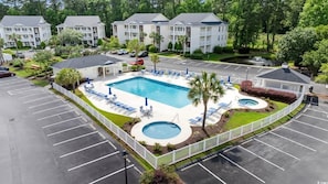 A hotel with a swimming pool, lounge chairs, and a parking lot.