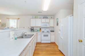 Cocina compacta con armarios blancos, microondas, estufa y refrigerador.