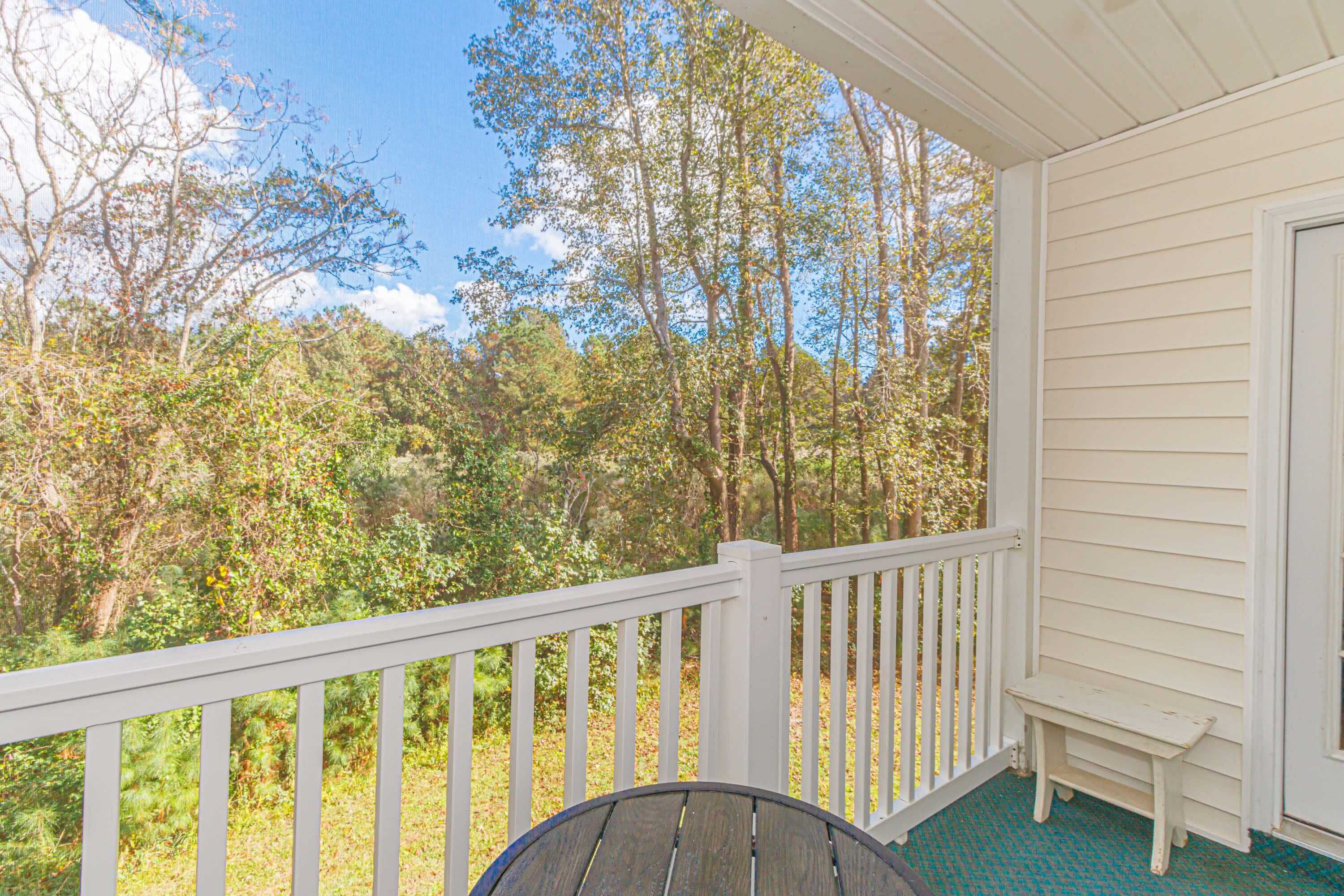 A porch with a white railing, a small bench, and a view of a forested area.