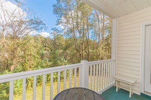 A porch with a white railing, a small bench, and a view of a forested area.