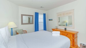 Quarto de hotel com uma cama, cômoda, espelho, janela com cortinas e abajur.