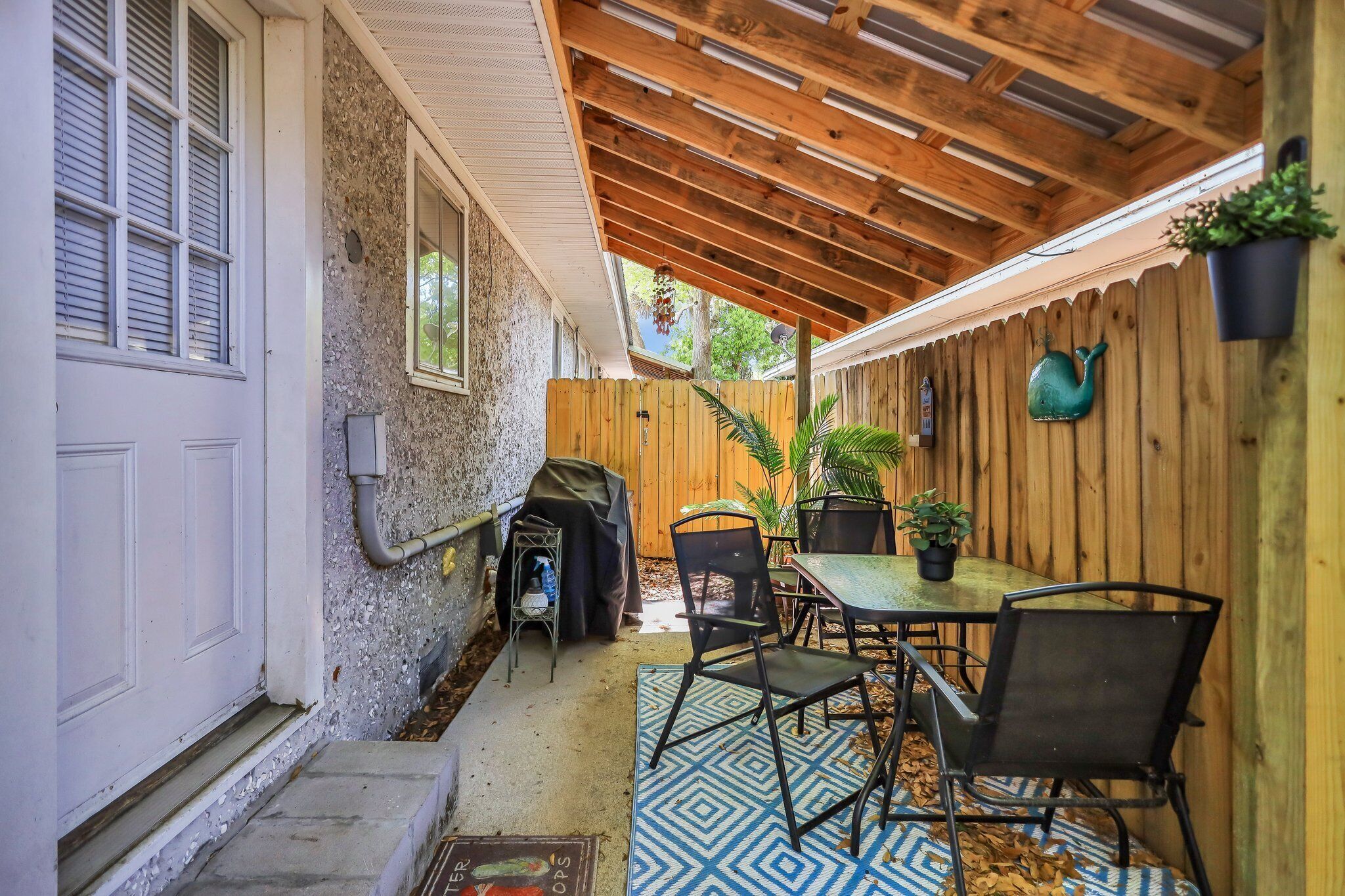 Une terrasse couverte avec un plafond en bois, une table et des chaises, une plante en pot et une clôture en bois.