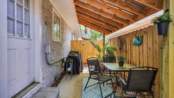 Une terrasse couverte avec un plafond en bois, une table et des chaises, une plante en pot et une clôture en bois.