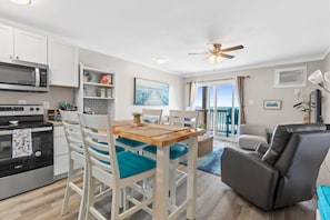 Una cocina moderna con armarios blancos, un microondas y un horno. Hay una mesa de comedor con sillas y un ventilador de techo.