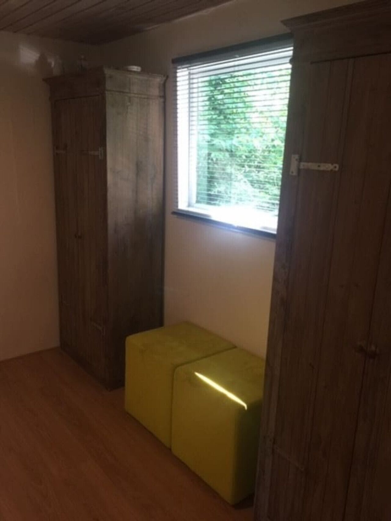 Une pièce avec des armoires en bois, un banc et une fenêtre avec des stores.