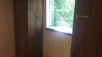 A room with wooden wardrobes, a bench, and a window with blinds.