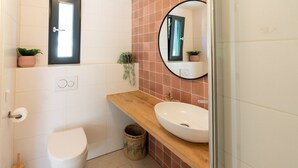 A modern bathroom with a white toilet, a wooden vanity with a white sink, and a round mirror. - Hytte, which is Norwegian for cabin or (wooden) house in nature. (Epe)