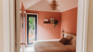 A bedroom with a bed, a window, a door, and a shelf with items. - Hytte, which is Norwegian for cabin or (wooden) house in nature. (Epe)