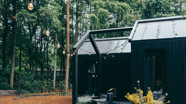 A modern outdoor deck with a black metal roof, surrounded by a forest. - Mysa Tiny House. At MYSA, every day feels as relaxed as a Sunday morning. (Epe)