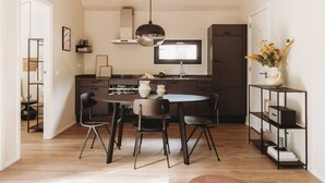 A modern kitchen with a dining table and chairs, a hanging light fixture, and a built-in oven. - Mysa Tiny House. At MYSA, every day feels as relaxed as a Sunday morning. (Epe)