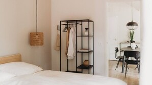 A bedroom with a bed, a hanging basket, a black metal wardrobe, and a dining area with a table and chairs. - Mysa Tiny House. At MYSA, every day feels as relaxed as a Sunday morning. (Epe)