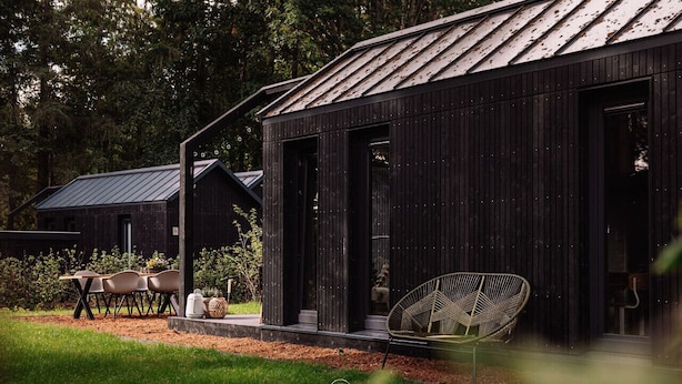 A modern building with a dark exterior, large windows, and a visible outdoor seating area with chairs and a table. - GrØn Tiny House in the forest (Epe)