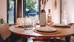 A dining table set with plates, a glass pitcher, and a bottle of mezze corona wine. - GrØn Tiny House in the forest (Epe)