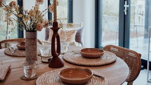 A dining table with woven placemats, a candle holder, and a vase of flowers. - WØUD cabin in the forest (Epe)