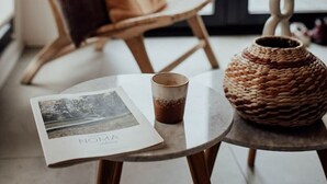 A cozy room with a wooden rocking chair, a small table with a cup and a book, and a woven basket. - WØUD cabin in the forest (Epe)