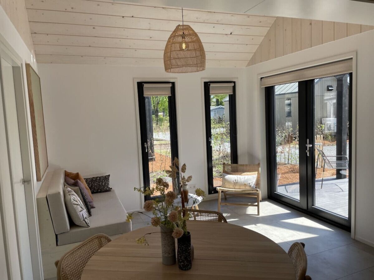 Un interior moderno con zona de comedor, sofá con cojines y vistas a un patio exterior a través de puertas de cristal amplias.