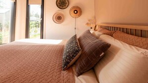 A neatly made bed with a patterned bedspread, a quilted pillow, and a wooden headboard. - WØUD cabin in the forest (Epe)