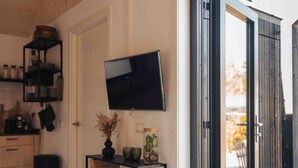 Una cocina moderna con un televisor de pantalla plana montado en la pared, una consola negra con adornos y una puerta que da a un área exterior.