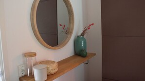 Une étagère en bois avec un miroir, un vase turquoise orné de fleurs rouges et deux paniers tressés.