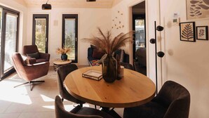 Un espace repas moderne avec une table ronde en bois, des chaises à l’assise rembourrée de couleur sombre et un vase contenant des plantes séchées.