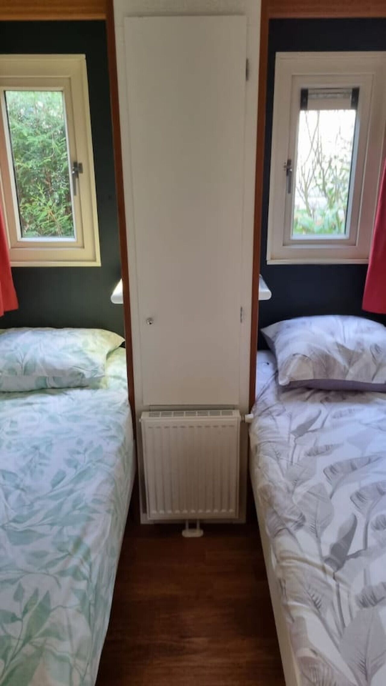 Una habitación con dos camas, un radiador y ventanas con cortinas.