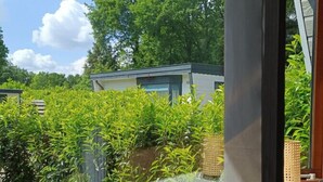 Vista de uma varanda com guarda-corpo de vidro, com vista para um jardim com plantas variadas e um cacto.