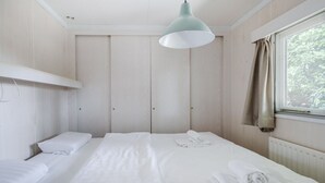 Un dormitorio con una cama individual, una lámpara colgante, una ventana con cortinas y un radiador.