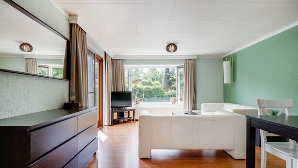 Una sala de estar moderna con un ventanal grande, un televisor de pantalla plana, un sofá blanco y un aparador de madera.